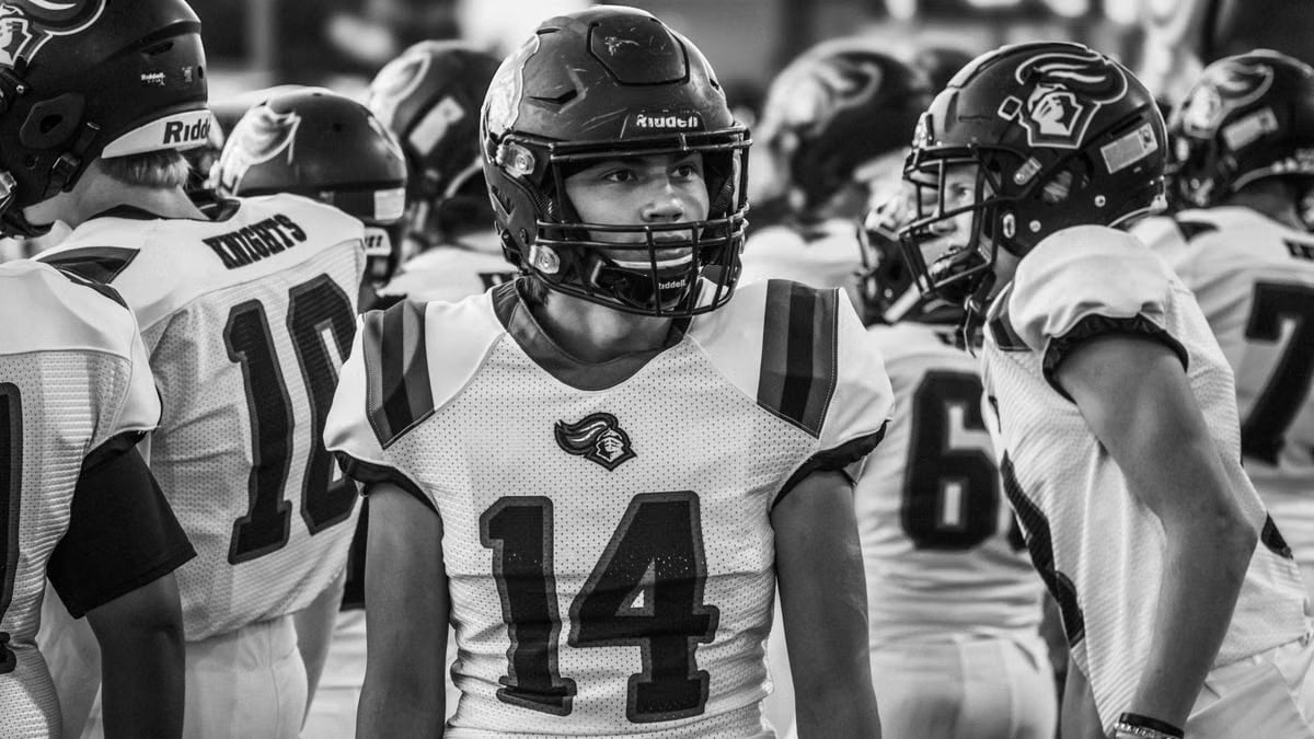 Black and white photo of a high school football team preparing for their game, showcasing teamwork and anticipation.