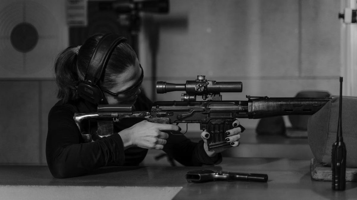 Woman aiming rifle in shooting range. Black and white focus on precision and skill.